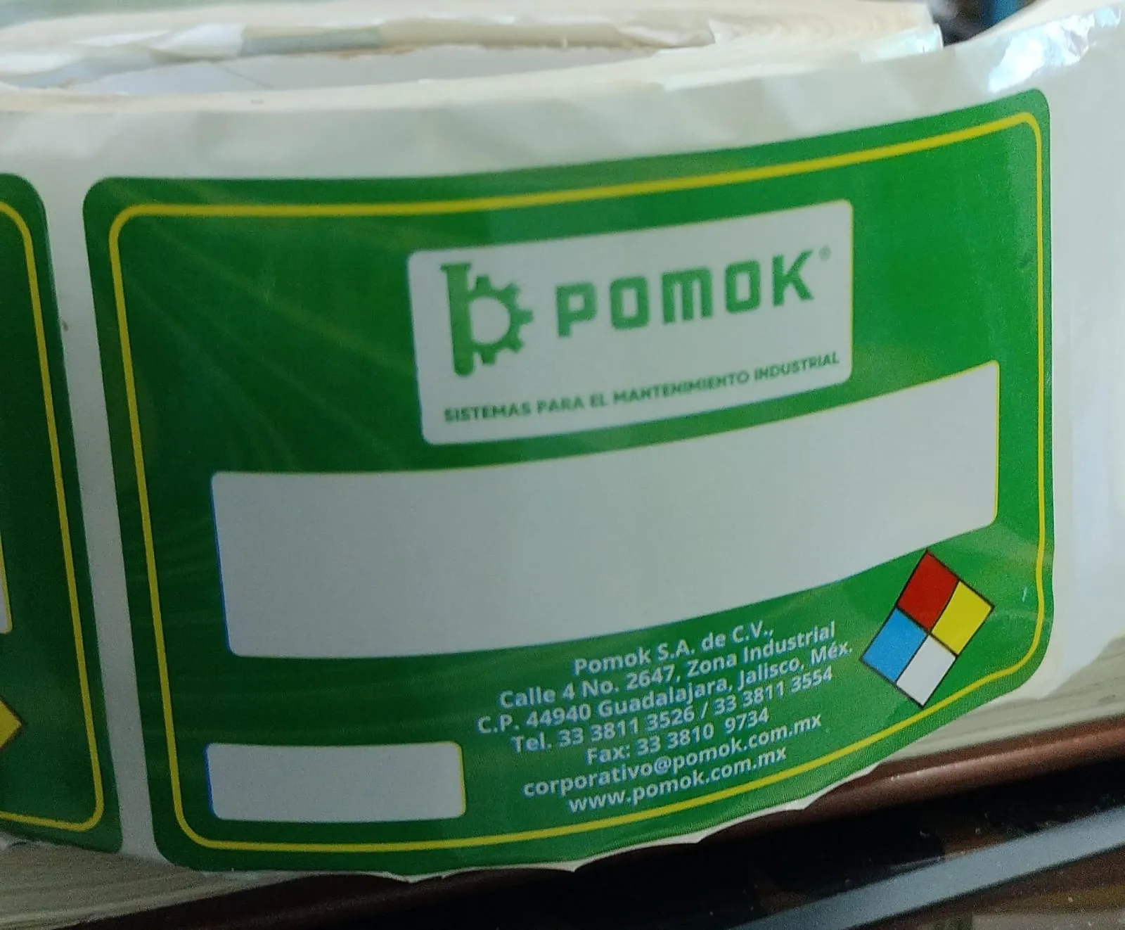 Fábrica de etiquetas: Fotografía de un rollo blanco de etiquetas color verde con letras color blanco y detalles de colores.